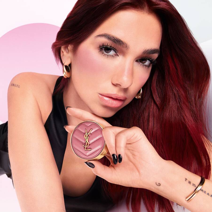 High-fashion campaign image featuring a model with bold pink blush, holding the YSL Make Me Blush Bold Blurring Blush compact