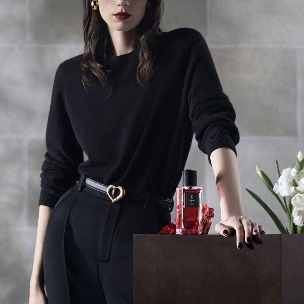 A model's dressed in black, posing next to the COEUR fragrance bottle for YSL Beauty.