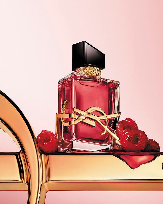Libre Berry Crush perfume bottle with gold YSL logo, surrounded by raspberries on a soft pink background.