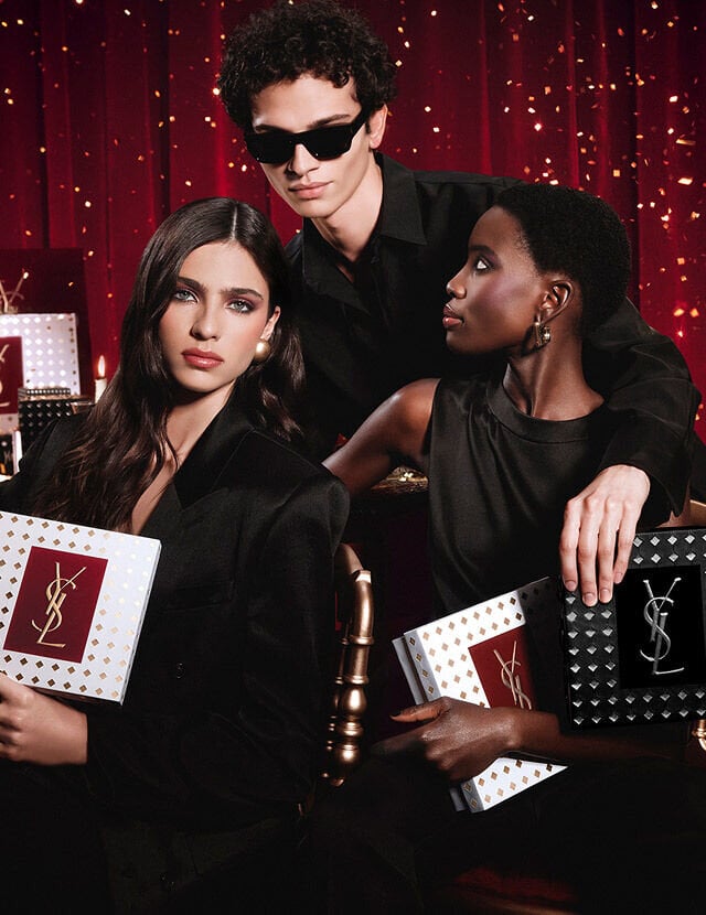 Models posing together holding luxury YSL Holiday gift boxes in a festive atmosphere.