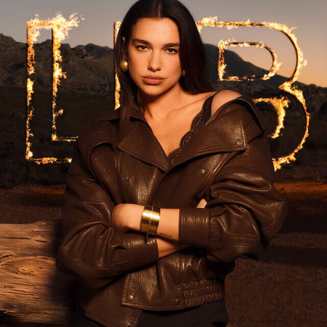 Dua Lipa in a brown leather jacket with large flaming LIBRE letters in a raw desert landscape.