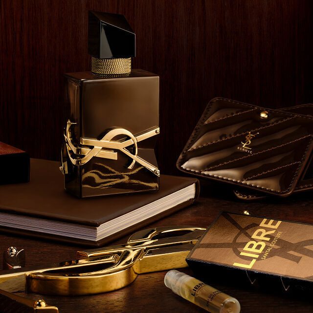 Libre Santal Couture bottle on a desk with a YSL leather pouch, a notebook, and a gold mirror.
