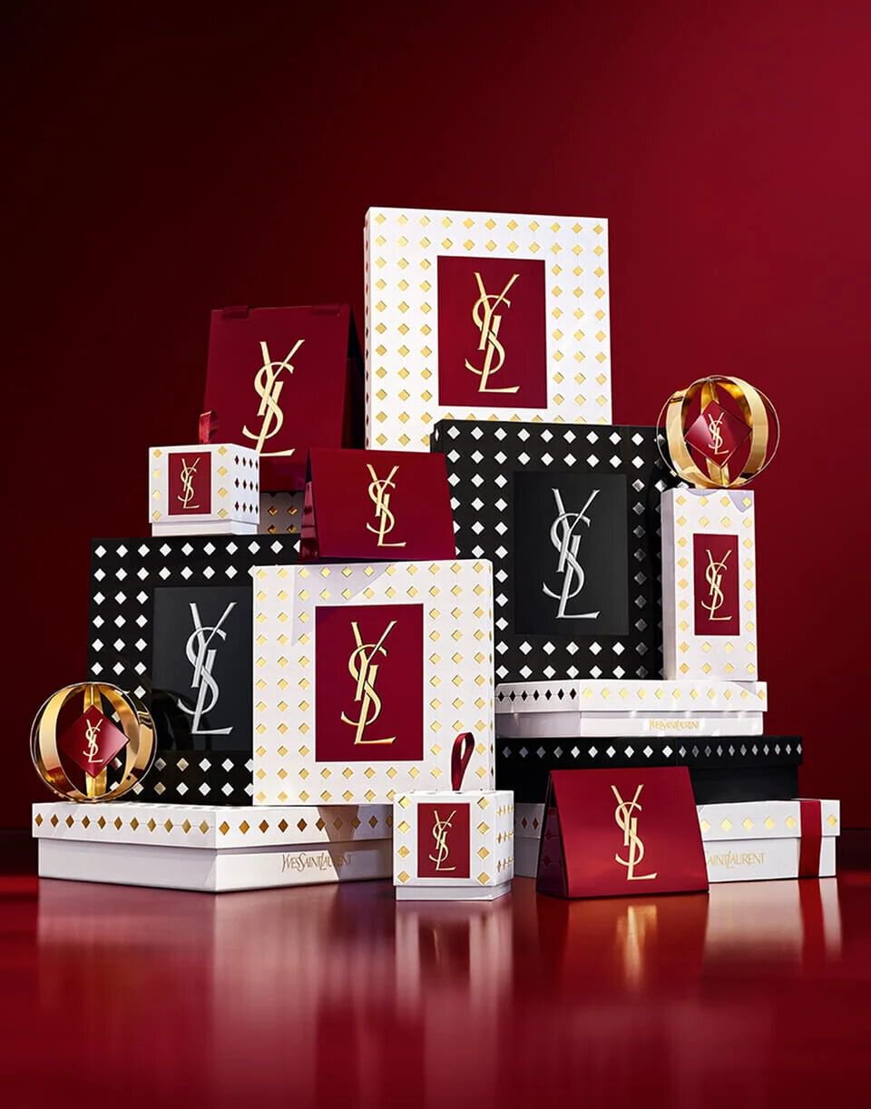 Assortment of luxury YSL Holiday gift sets elegantly displayed on a deep burgundy backdrop.
