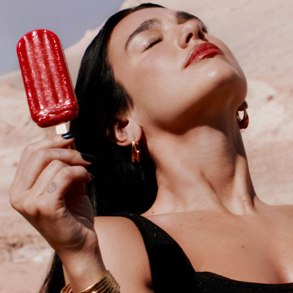 Dua Lipa, YSL Beauty ambassador, with red lips, holding a red popsicle, representing LIBRE Eau de Parfum Berry Crush
