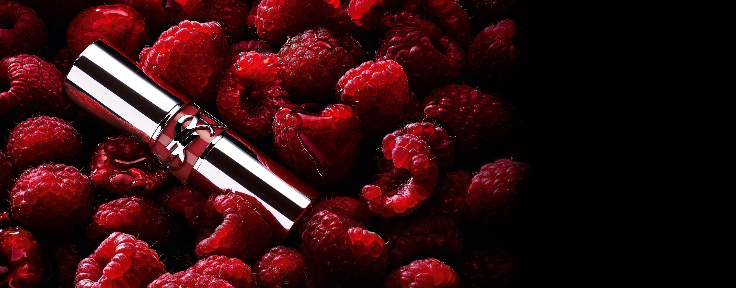 YSL LOVESHINE Berry Crush lipstick, silver tube with berry YSL logo, nestled among fresh raspberries.