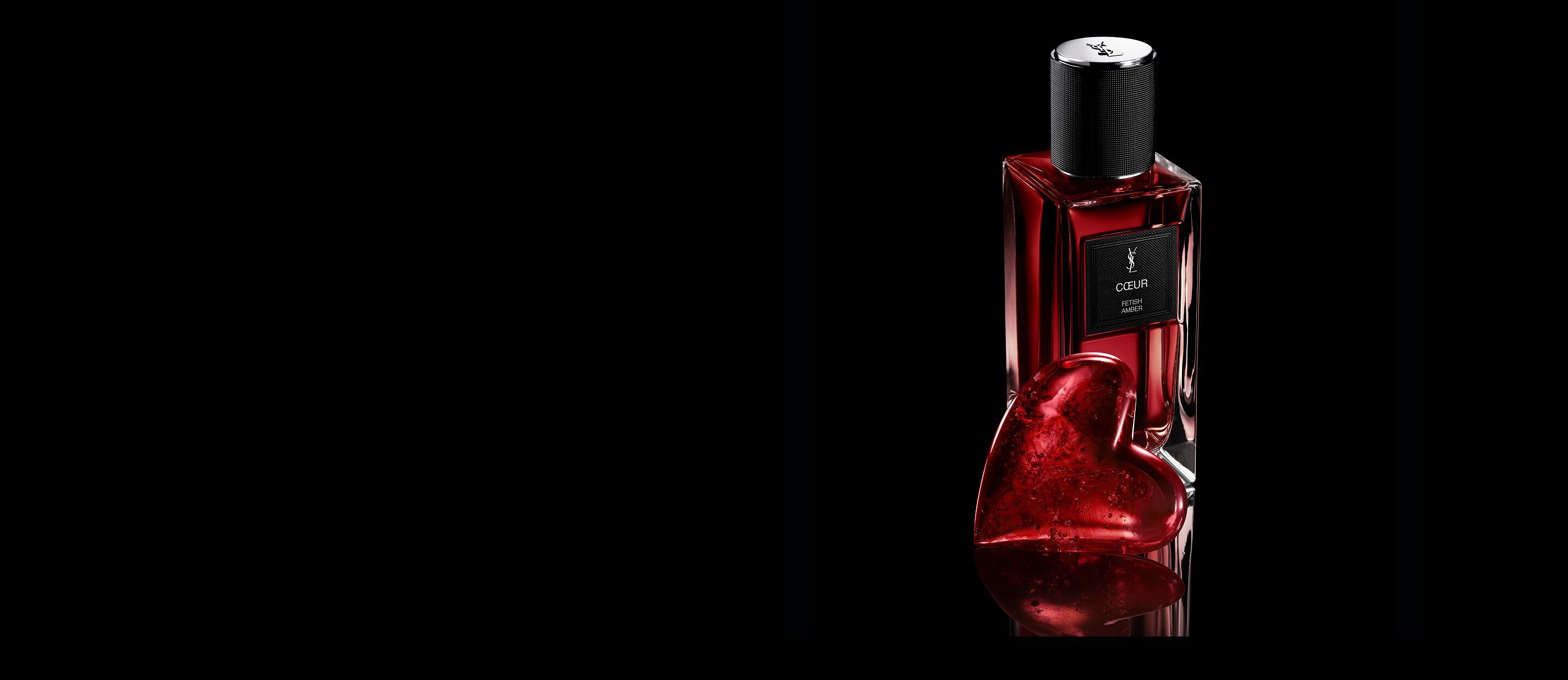 CŒUR Eau de Parfum by YSL bottle
next to a ruby-red heart jewel on a
reflective black surface.