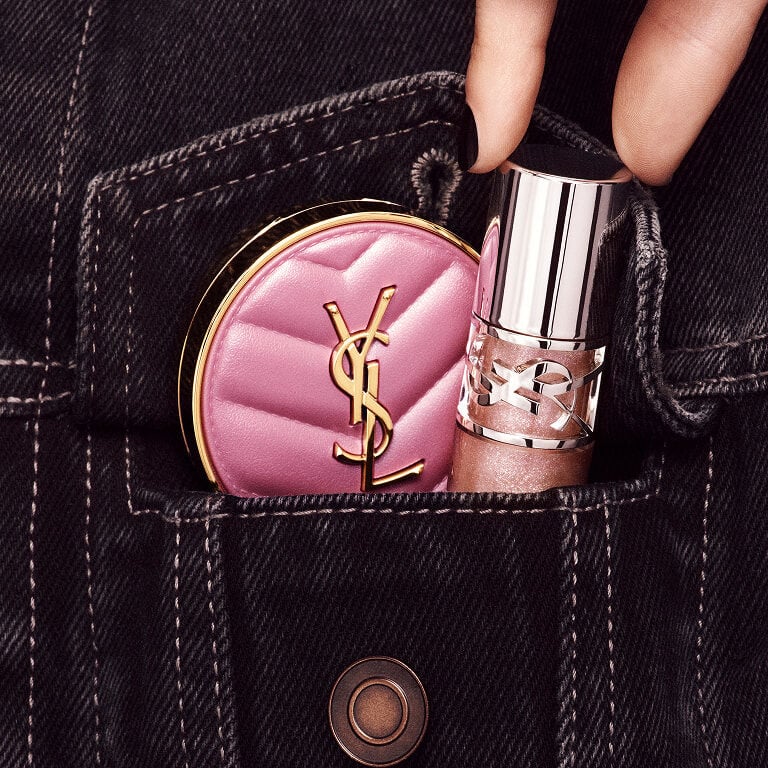 Hand placing YSL LOVESHINE Lip Oil Gloss and pink Make Me Blush
compact into a denim pocket in shade Stardust Love.