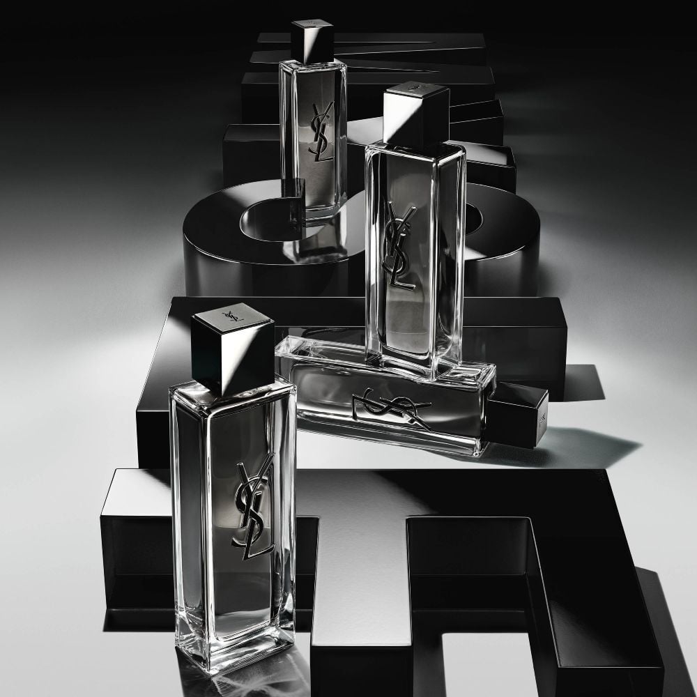 High-angle view of MYSLF Eau de Toilette Intense bottles arranged on large black 3D letters spelling MYSLF laid flat on the ground.