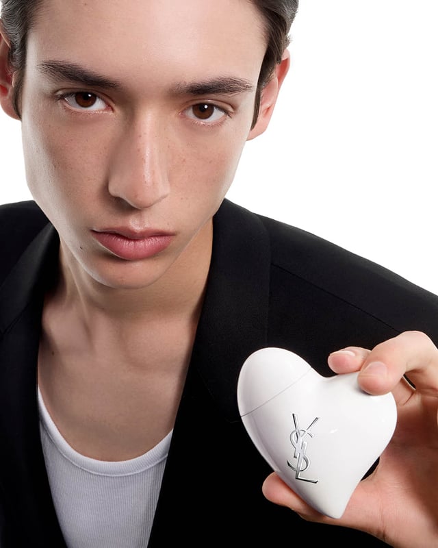 Close-up of a man in a black blazer holding the white heart-shaped CARE CRUSH product. White background.