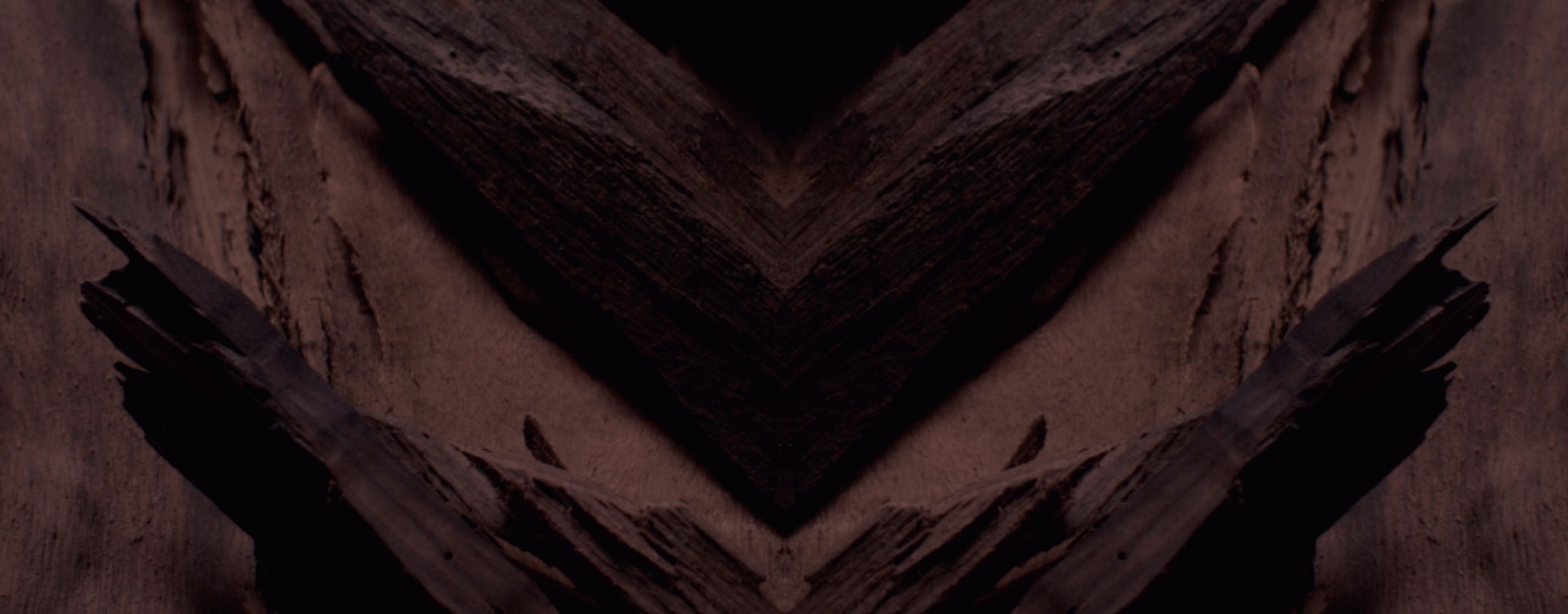 Dark, textured background with a prominent chevron pattern in
deep browns and blacks, designed for YSL LVP Extrait de Parfum
product display.