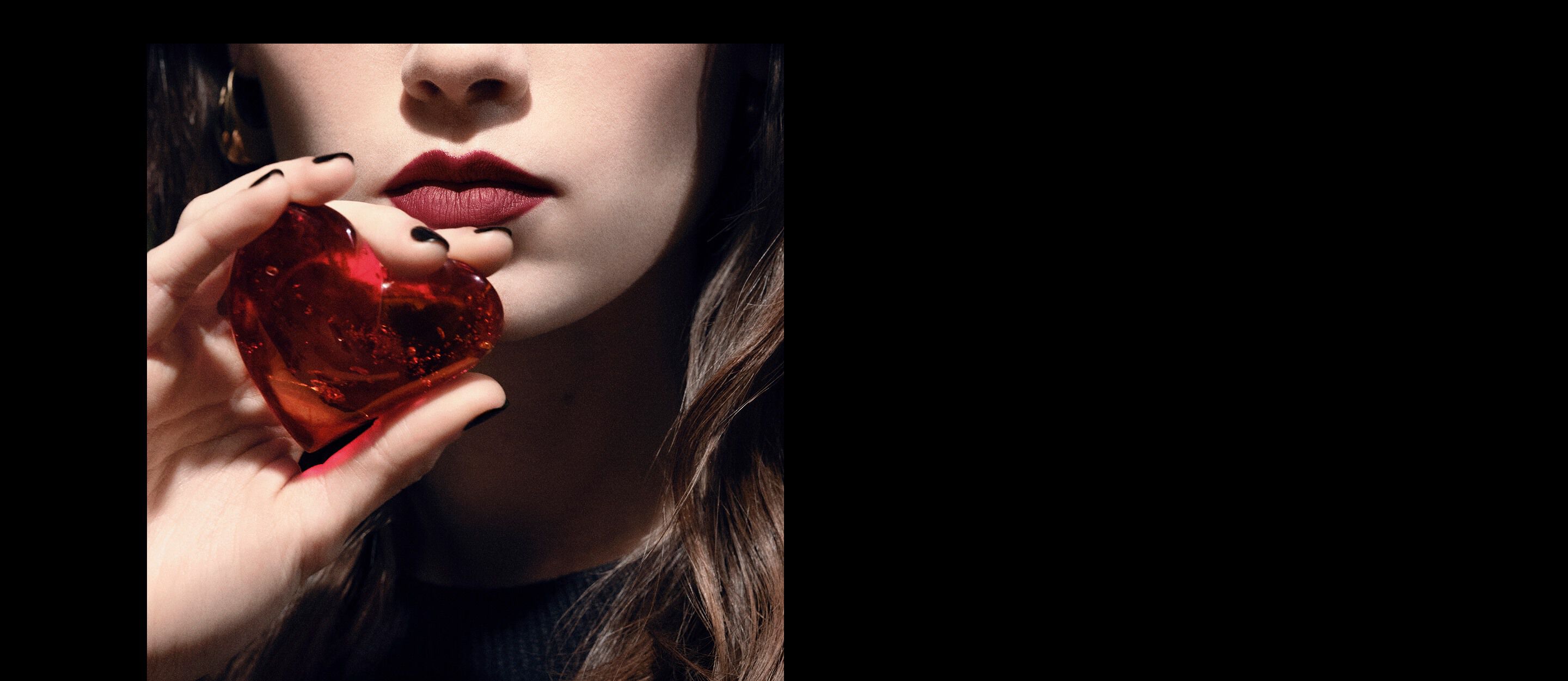 Close-up of a model's lips and hand
holding a translucent ruby-red heart
jewel for YSL CŒUR Eau de Parfum.