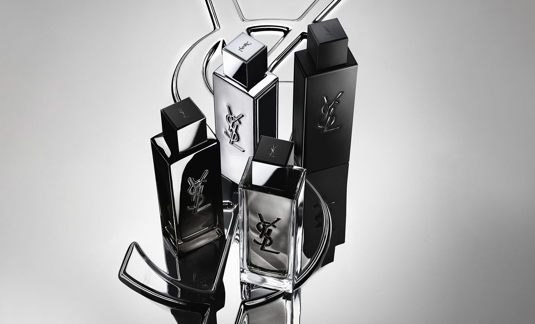 Group shot of the complete MYSLF fragrance range bottles standing on a large YSL Cassandre logo with a reflective mirror effect.